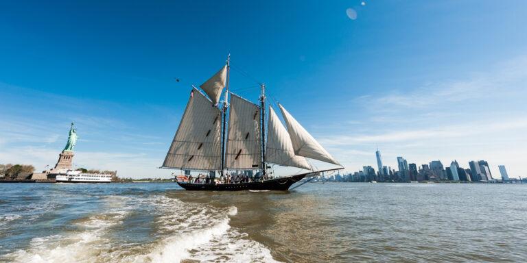 A schooner sailing in front of the Statue of Liberty.