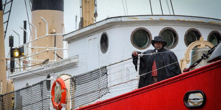 A person in costume standing on the deck of a red boat.