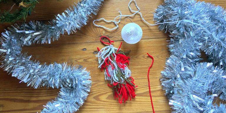 A hand-made yarn baggywrinkle in holiday colors on a wood surface with holiday tinsel.