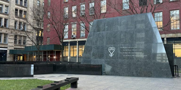 A large gray granite memorial with a poem etched into the surface in front of a red brick building.