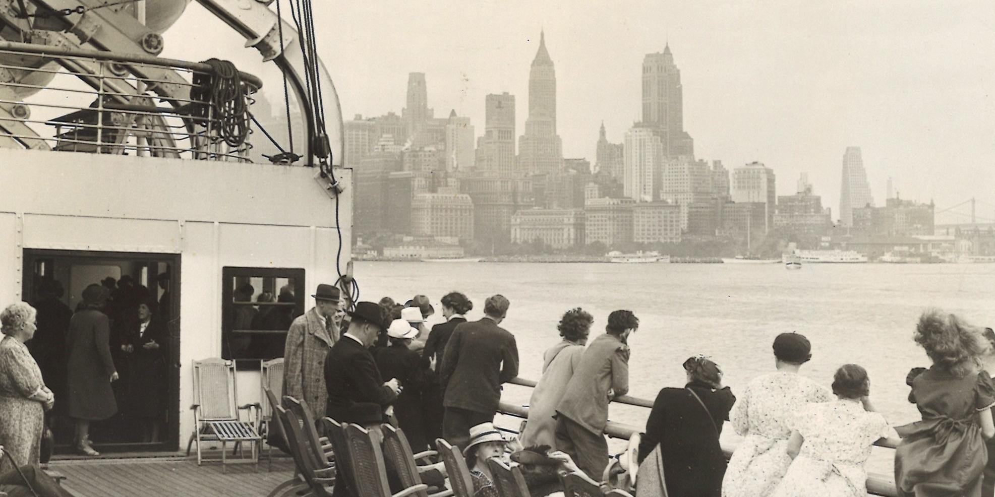 Black and white photograph depicting passengers aboard North German Lloyd Line ship SS Bremen looking starboard toward Manhattan skyline.