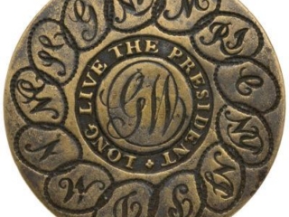 A round brass button featuring the initials &ldquo;GW&rdquo; in the center (for George Washington), surrounded by the words &ldquo;Long Live the President&rdquo;. Around the edge of the button are the initials of each of the 13 original colonies (states) linked together in circles.